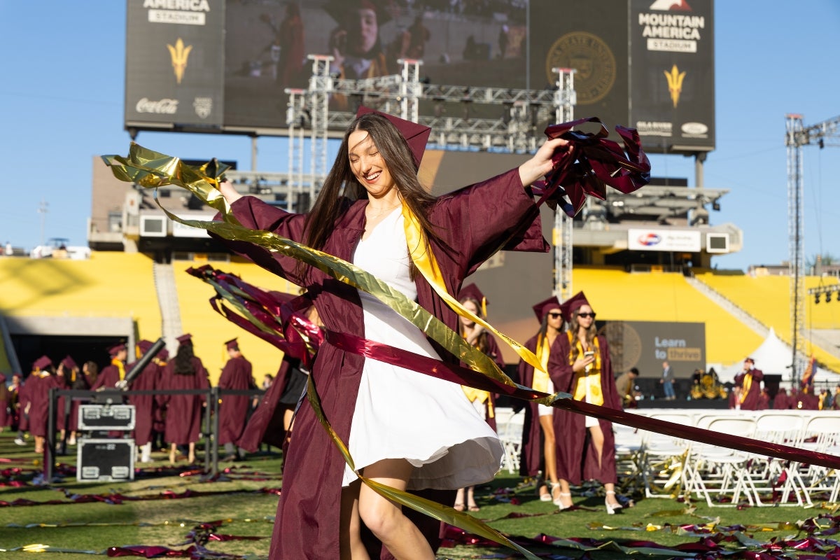 A woman in graduation regalia spins amid confetti streamers