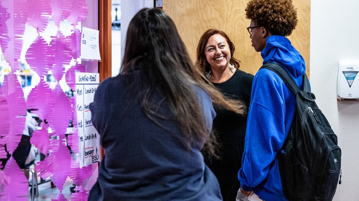 Woman greets two high school students at classroom door
