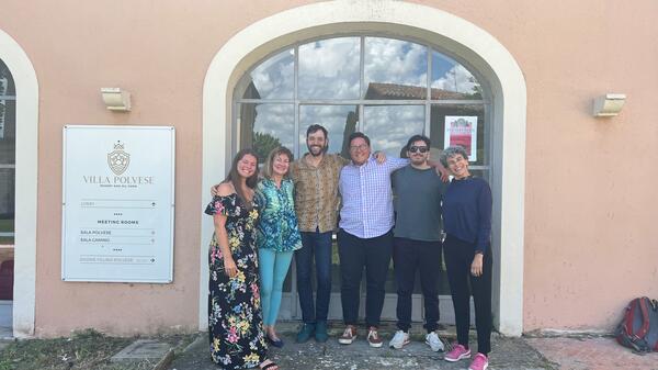 Five people pose together for a photo in front of an arched window.