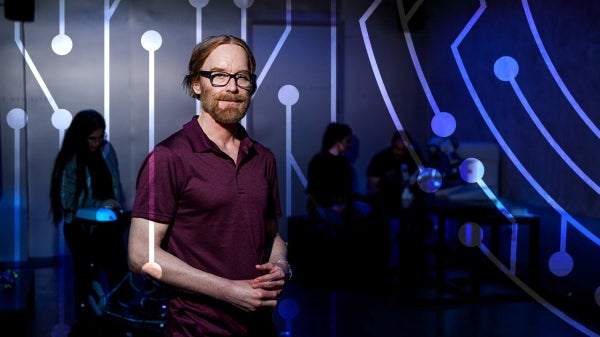 CHART director Jamie Gorman stands in a dimly lit room with circuit design graphics overlaid.