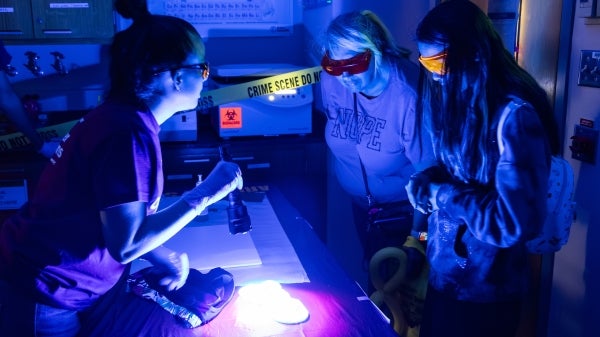 Three people with goggles on look at a table under a black light