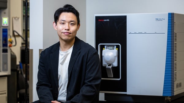 A male professor with short dark hair wearing a black blazer and a white t-shirt sits next to an ambient mass spectrometer 