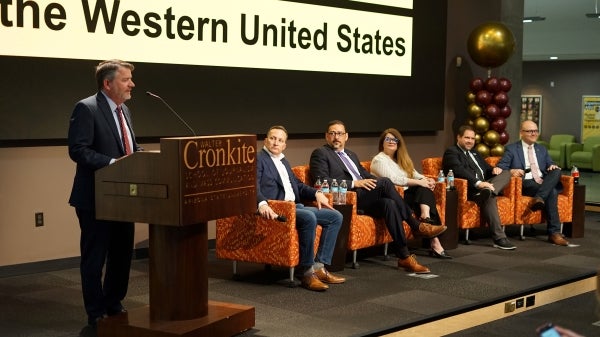 Person at a podium onstage next to five other seated panelists
