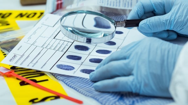 Gloved hands holding a magnifying glass up to fingerprints