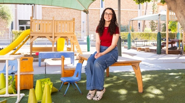 Sarah Nesbit sitting on a wooden bench in a playground with a canopy and play structure.