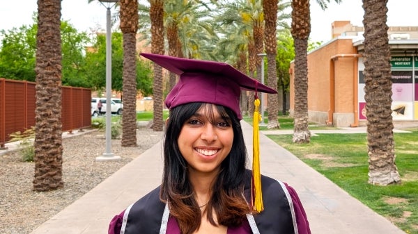 Ana Girish, 2025 spring grad, stands in her cap and gown on palm walk for a portrait shot.