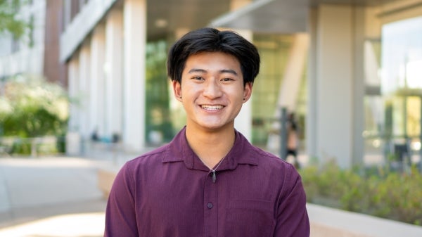 Vincent Truong, wearing a maroon shirt, smiles in front of ASU's Biodesign Institute Building B.