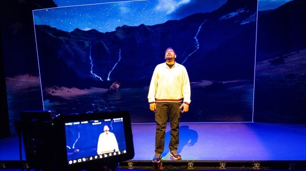 A man stands on a large stage with mountains projected on a screen